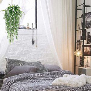 Hanging artificial white flowers with faux eucalyptus vine decor above a bed with patterned bedding.