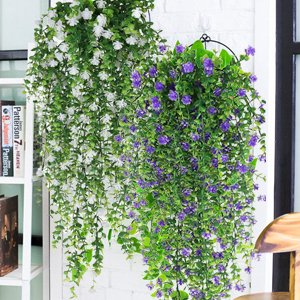 Two hanging baskets of artificial flowers and eucalyptus vines, one white and one purple, displayed outdoors.