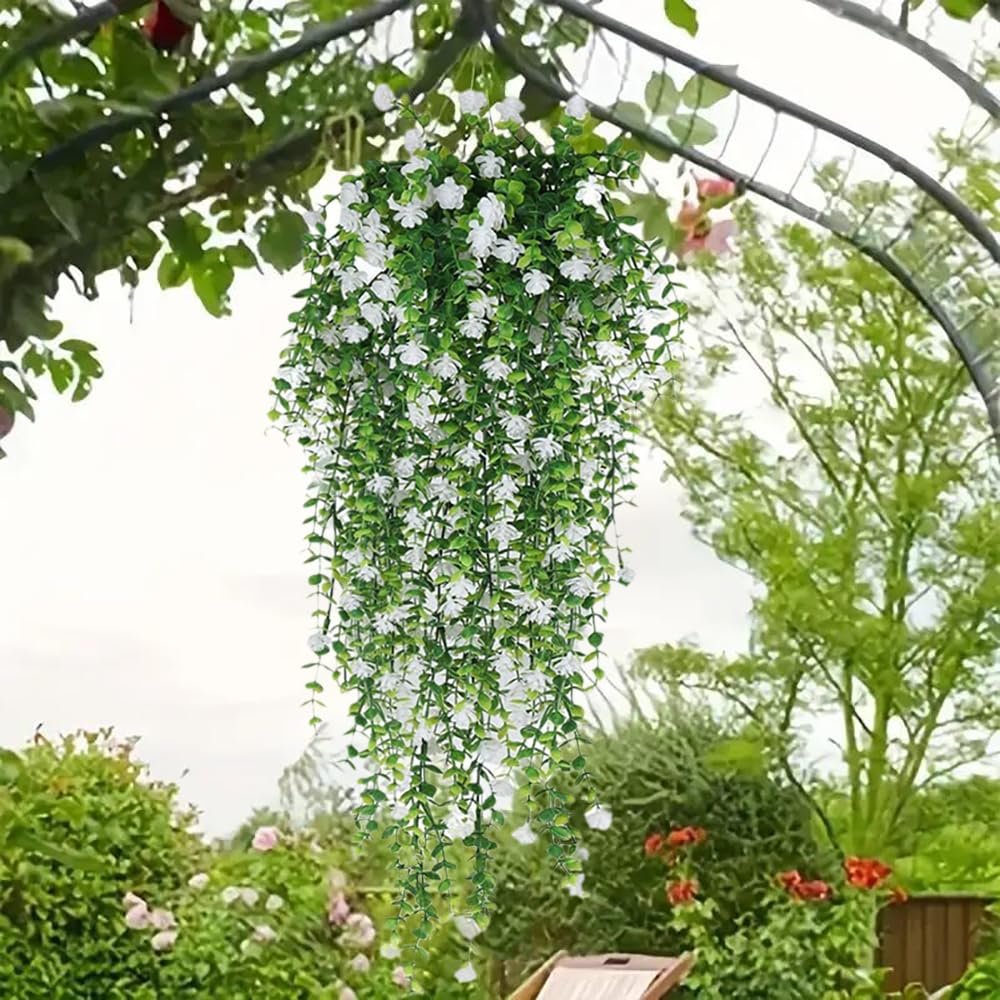 Artificial white flowers and eucalyptus vine hanging from an arbor in a garden setting.