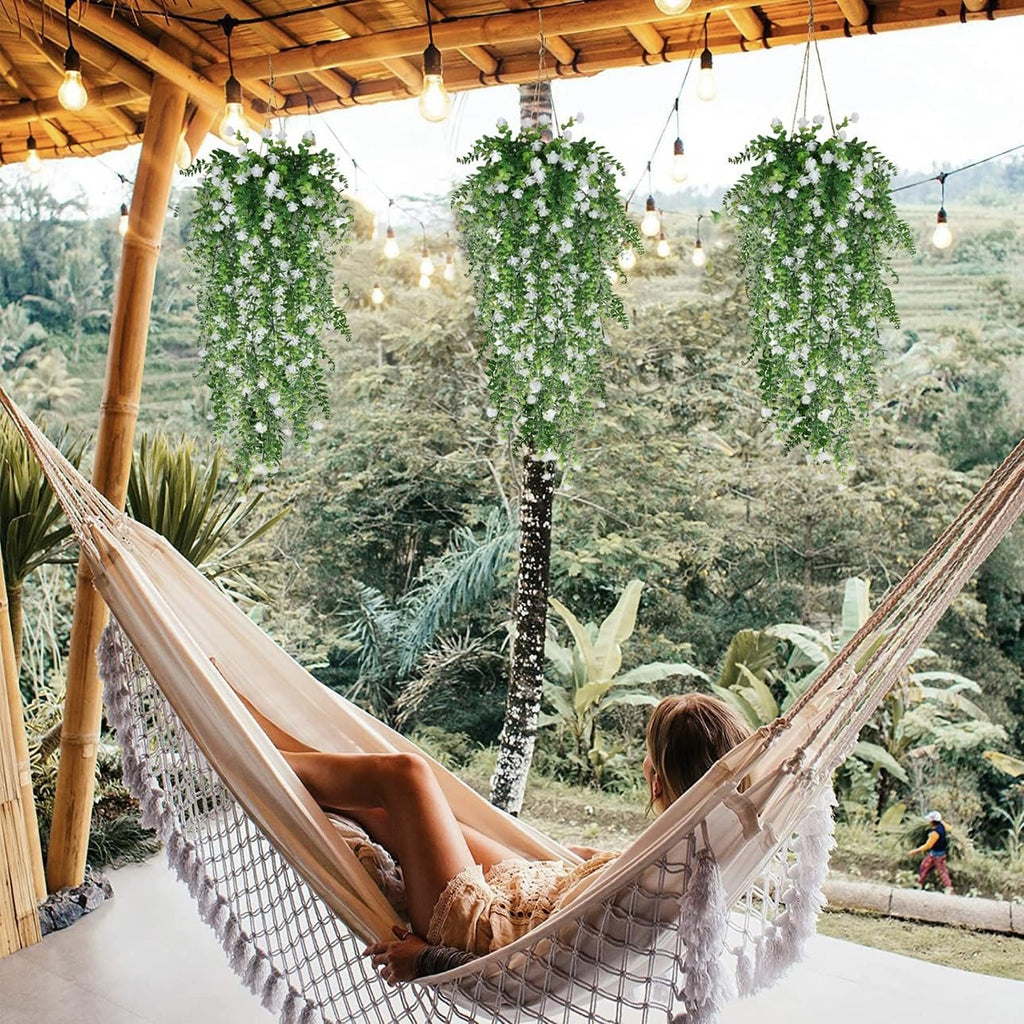 Woman relaxing in a hammock under a bamboo pergola with three hanging artificial white flower and eucalyptus vine garlands.