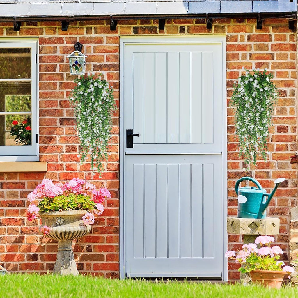 Two white artificial hanging flower garlands with faux eucalyptus vines decorating a brick wall next to a white door.