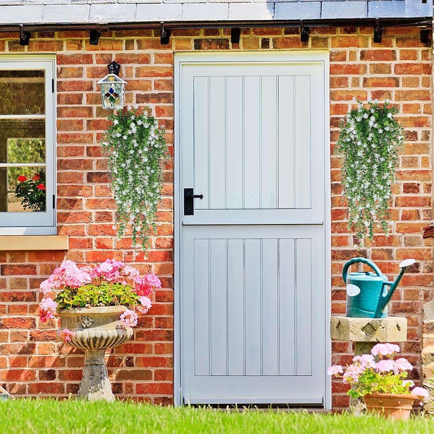 Two white artificial hanging flower garlands with faux eucalyptus vines decorating a brick wall next to a white door.