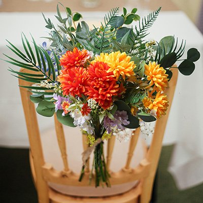 Artificial marigold silk flower bouquet with orange and yellow blooms tied with twine, resting on a wooden chair.