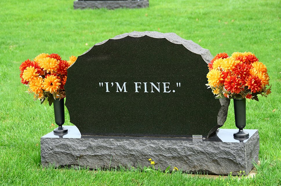 Headstone with artificial orange and yellow marigold bouquets on either side, inscribed with "I'M FINE."
