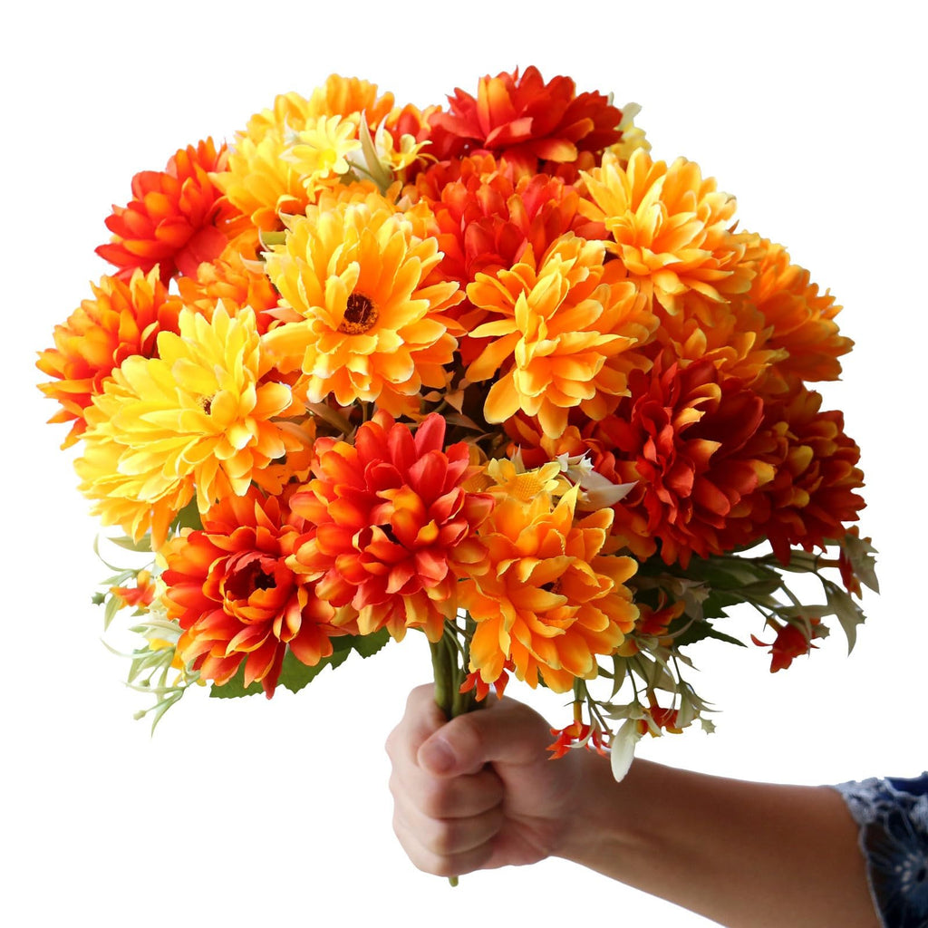 Hand holding a bouquet of artificial marigold silk flowers in burnt orange and yellow hues against a white background.