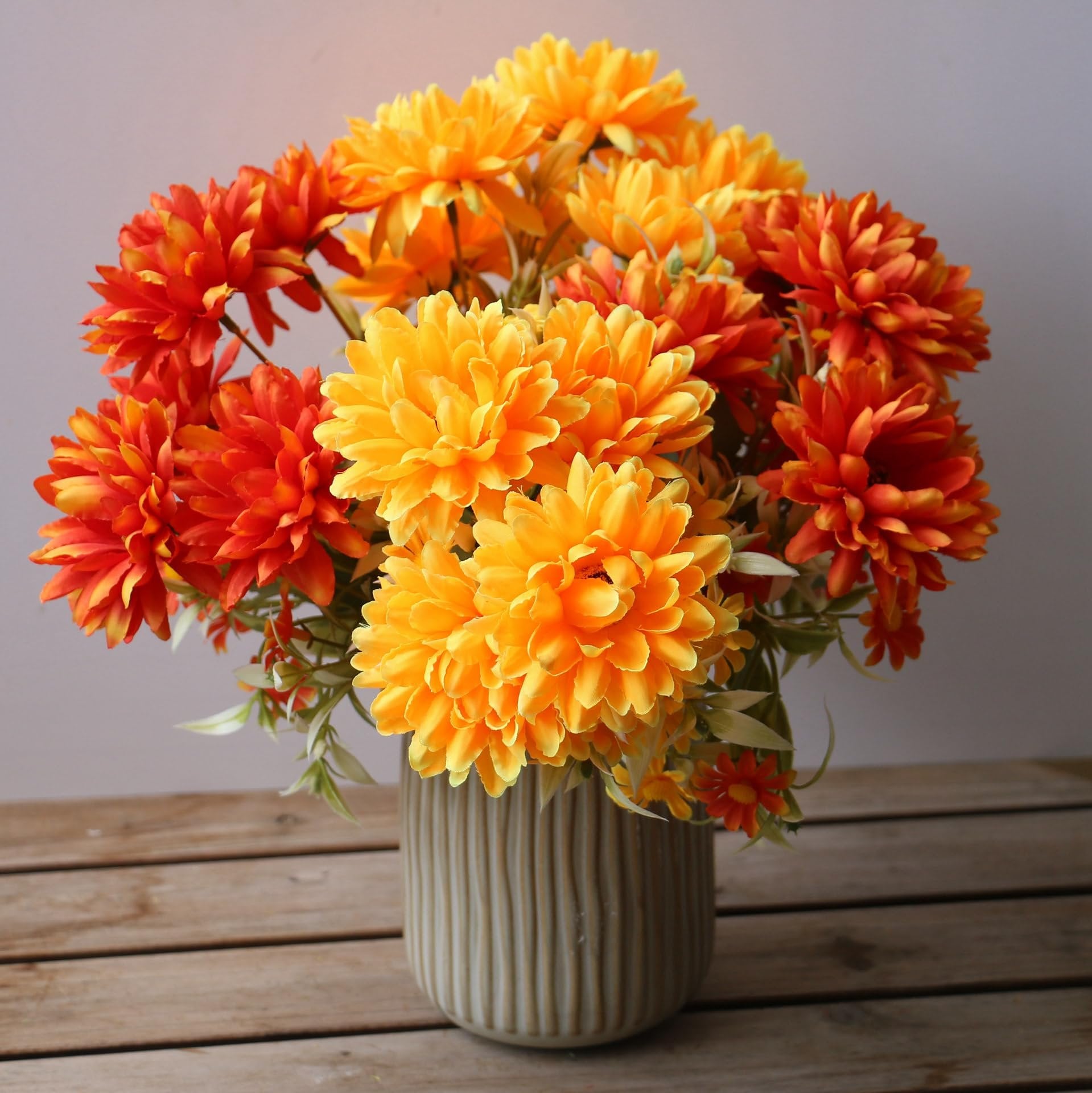 Artificial marigold silk flower bouquets in burnt orange and yellow hues, arranged in a ribbed vase on a wooden surface.