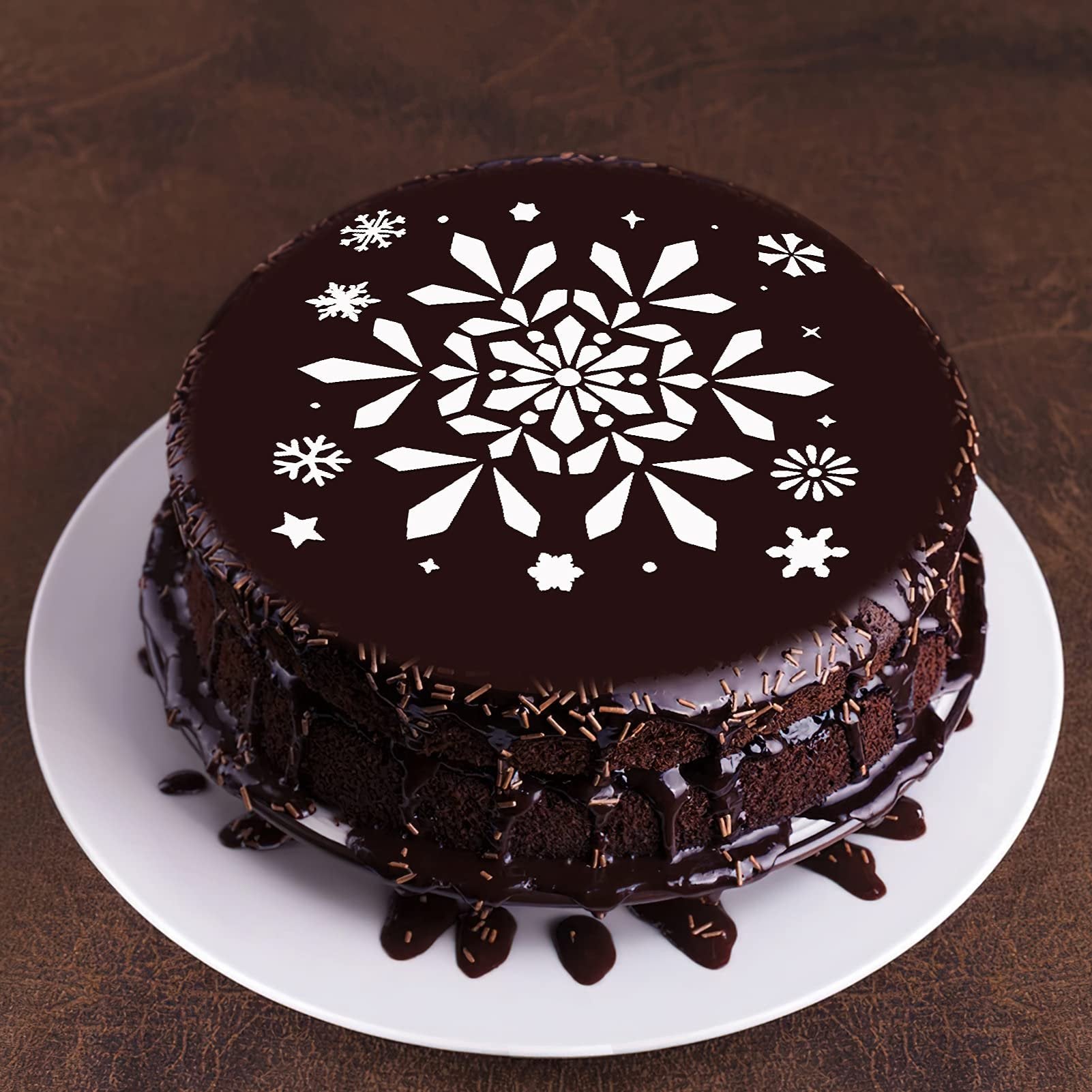 Chocolate cake decorated with white snowflake stencils on top and chocolate frosting dripping down the sides.
