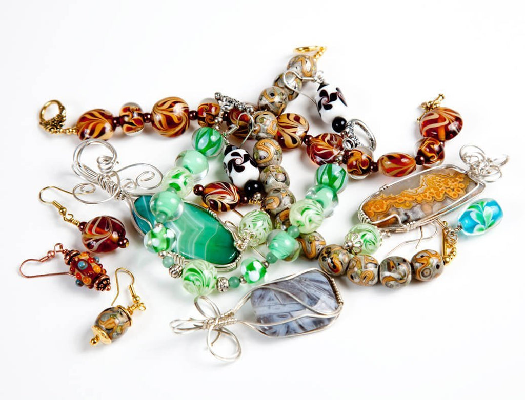 Assorted handmade jewelry including necklaces and earrings with colorful glass beads and pendants on a white background.