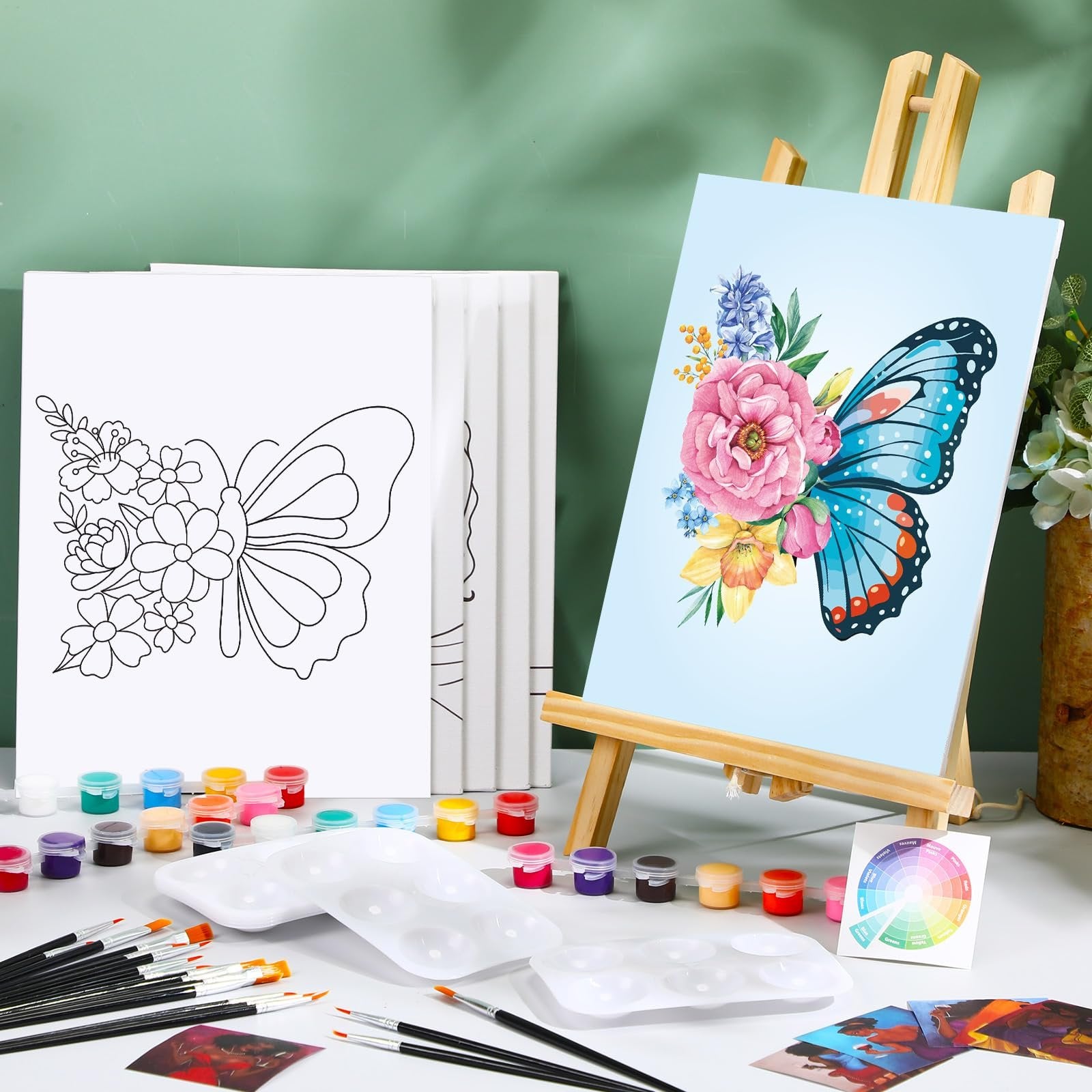 Butterfly painting kit contents including pre-drawn canvases, acrylic paints, brushes, and palettes on a white surface.