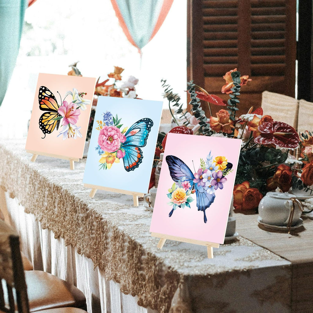Three pre-drawn butterfly painting canvases displayed on easels on a decorated table.