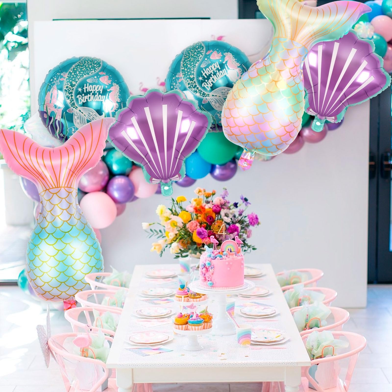 Mermaid tail, shell, and round balloons decorating a birthday party table with a pink cake and cupcakes.