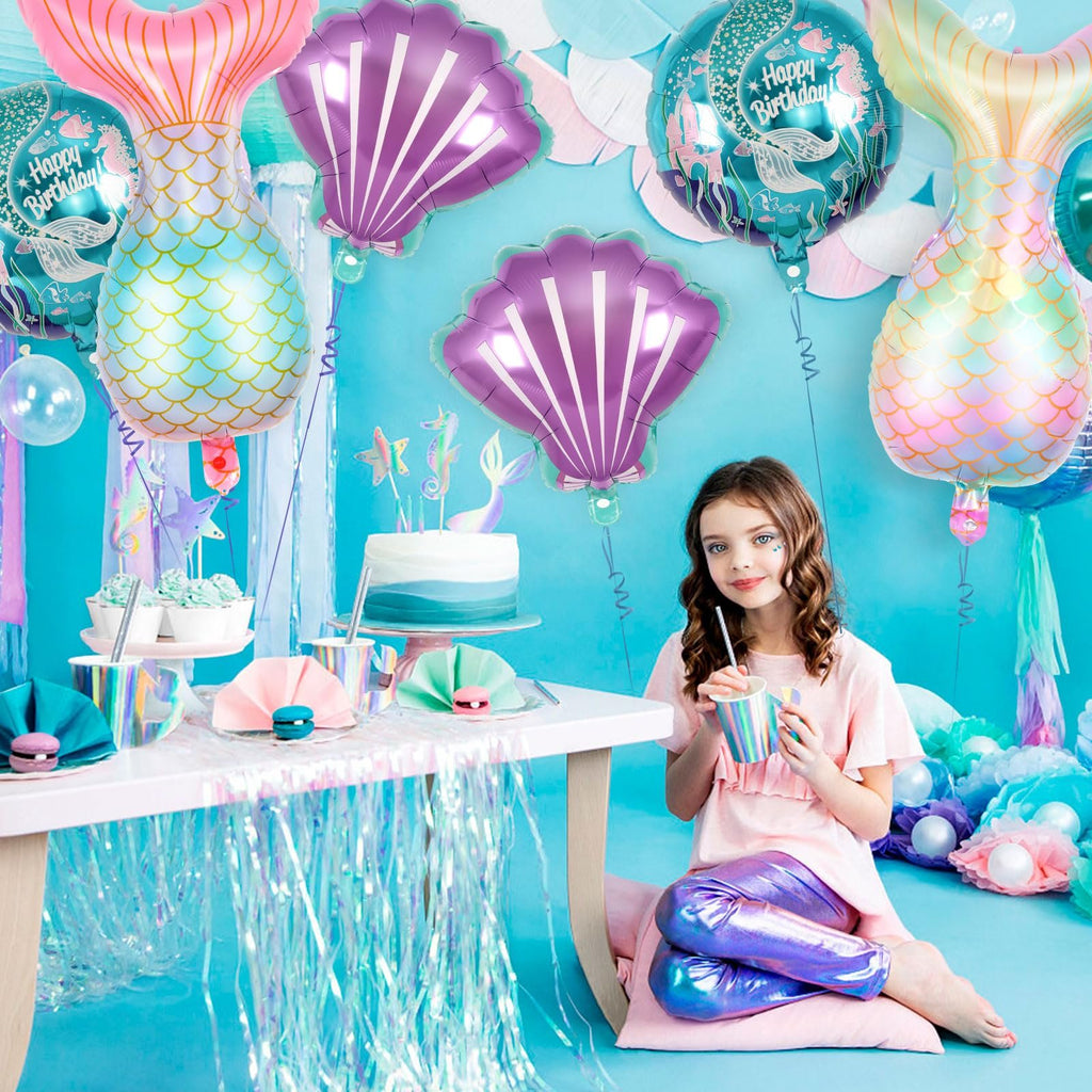 Girl at mermaid-themed birthday party with tail, shell, and round balloons, cake, and cupcakes