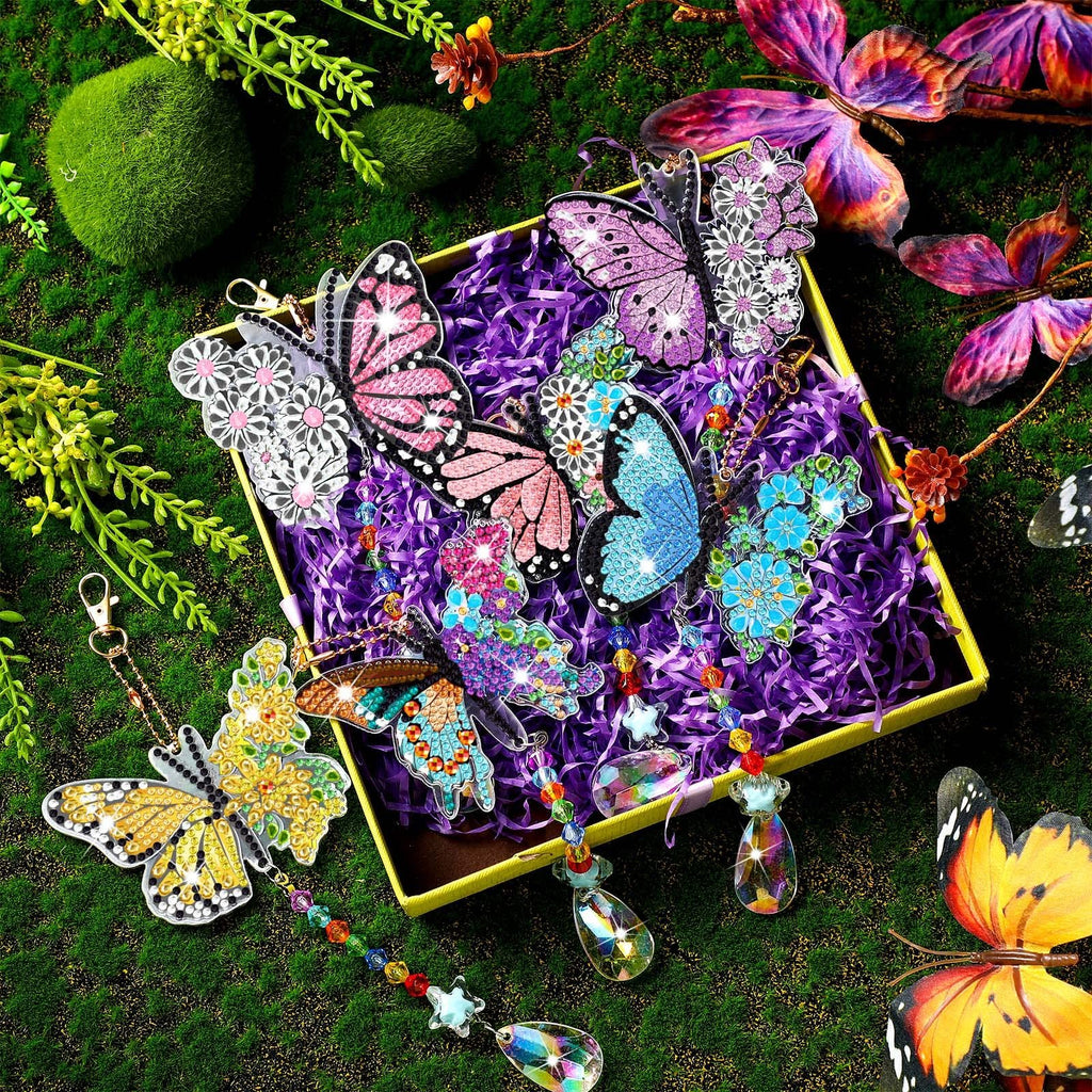 Diamond painting butterfly wind chimes and suncatchers displayed in a yellow box with purple shred, surrounded by greenery and decorative butterflies.