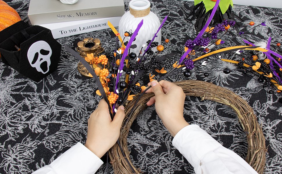 Hands arranging black floral picks with orange and purple berries onto a grapevine wreath for Halloween decor.