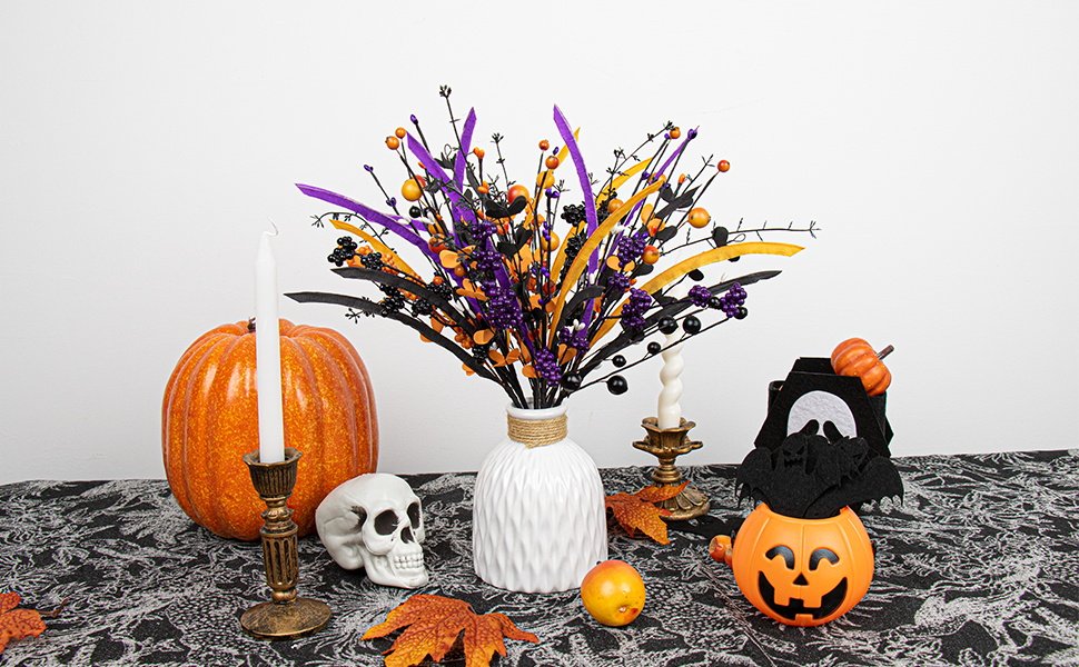 Halloween floral arrangement with black stems, purple and orange berries, and decorative leaves on a table with pumpkins and a skull.
