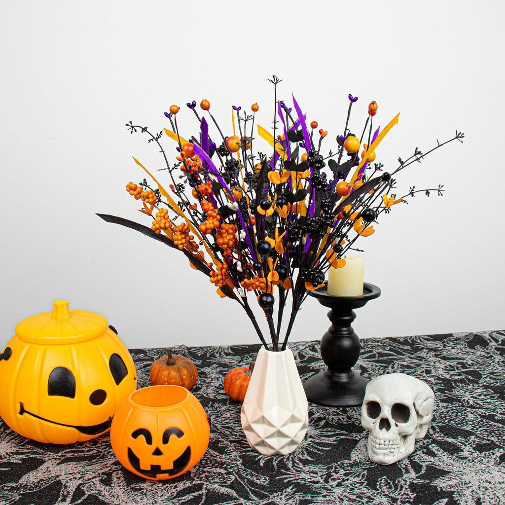 Halloween floral arrangement with black stems, orange berries, purple and yellow accents, in a white vase, with pumpkins, a skull, and a candle holder on a patterned tablecloth.