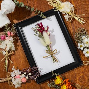 Assortment of mini dried flower bouquets arranged around a black picture frame on a wooden surface.