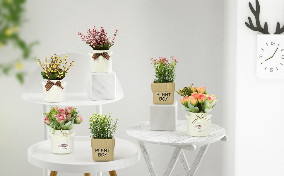 Six artificial floral arrangements in ceramic pots displayed on white tables, with a clock on the wall.