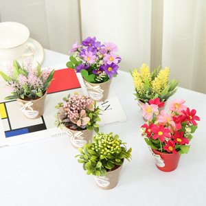 Six artificial flower arrangements in ceramic and metal pots on a white surface with a book and cup in the background.
