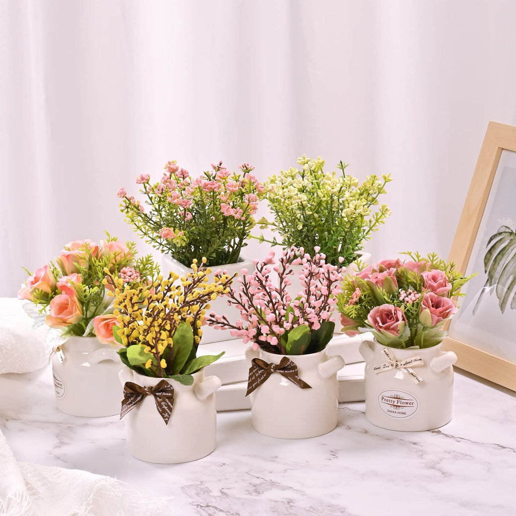 Six artificial floral arrangements in white ceramic pots with ribbons, displayed on a marble surface.