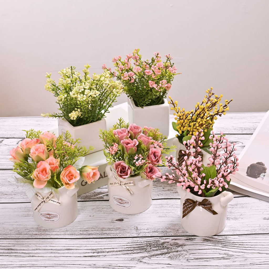 Five artificial floral arrangements in ceramic pots on a wooden surface.