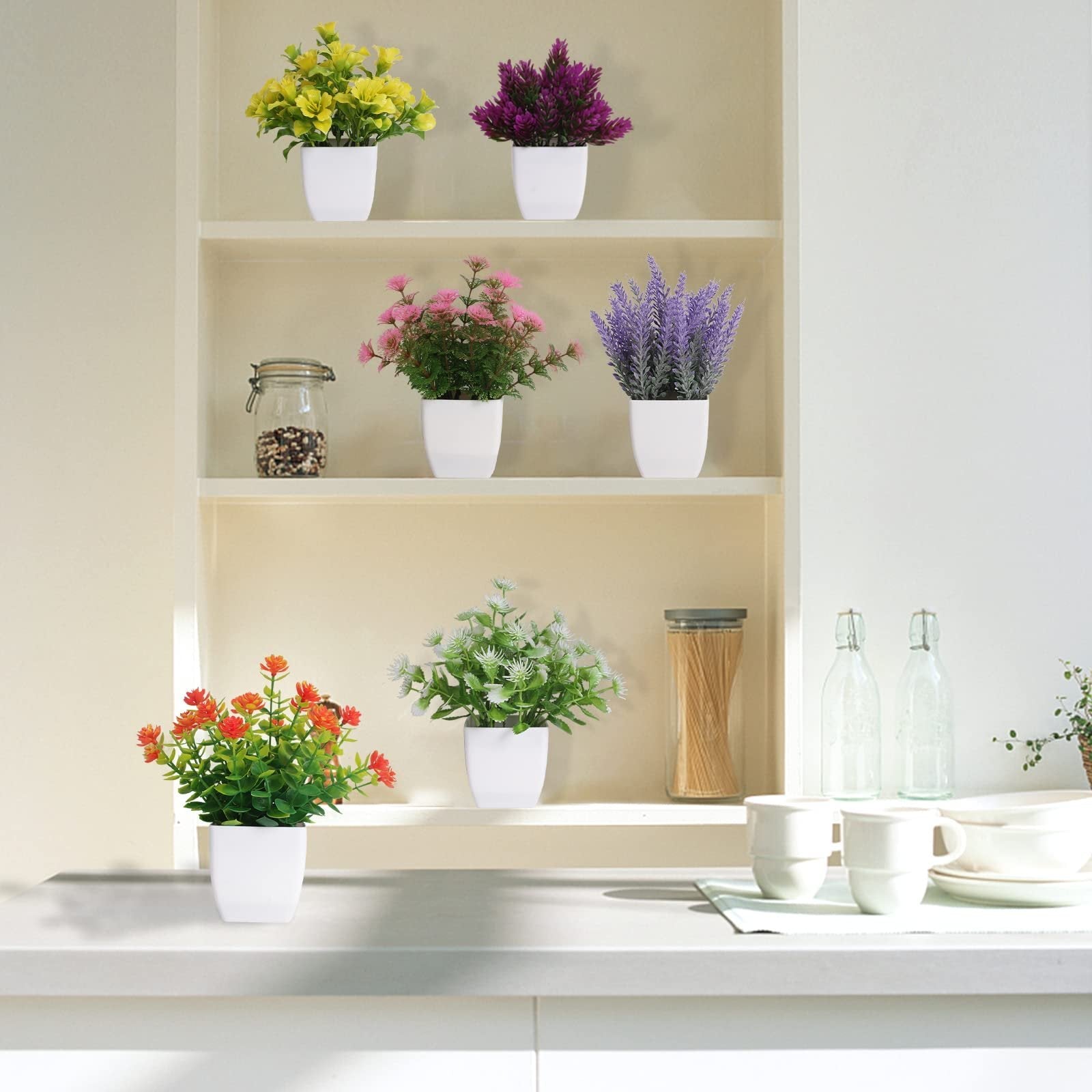 Six artificial potted plants in white pots arranged on kitchen shelves and countertop