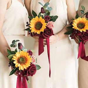Three bridesmaids holding artificial sunflower and rose bouquets with burgundy ribbons.