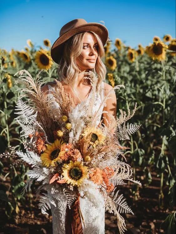 Woman in a hat holding a large bouquet of sunflowers and dried flowers in a sunflower field
