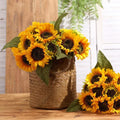 Artificial sunflowers in a woven basket and a separate bouquet on a wooden table.