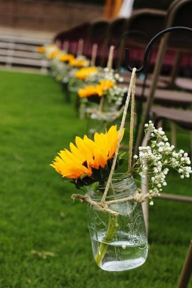 Artificial sunflowers and baby's breath in mason jar hanging from chair at outdoor event