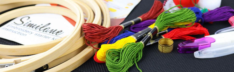 Embroidery starter kit with wooden hoops, colorful embroidery floss, thimble, and scissors on a black textured surface.
