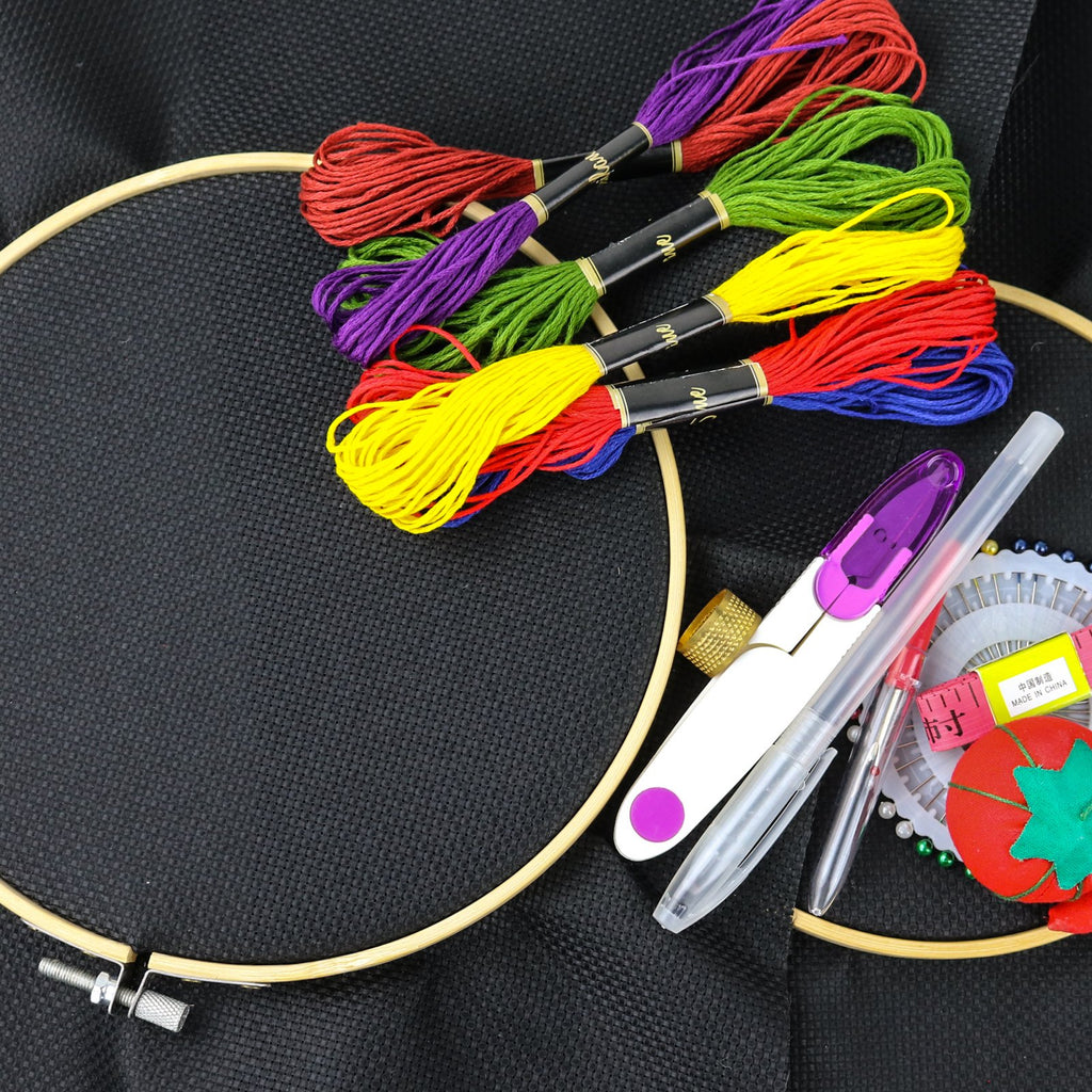 Embroidery kit with colorful threads, hoops, scissors, thimble, pins, and measuring tape on black Aida cloth.