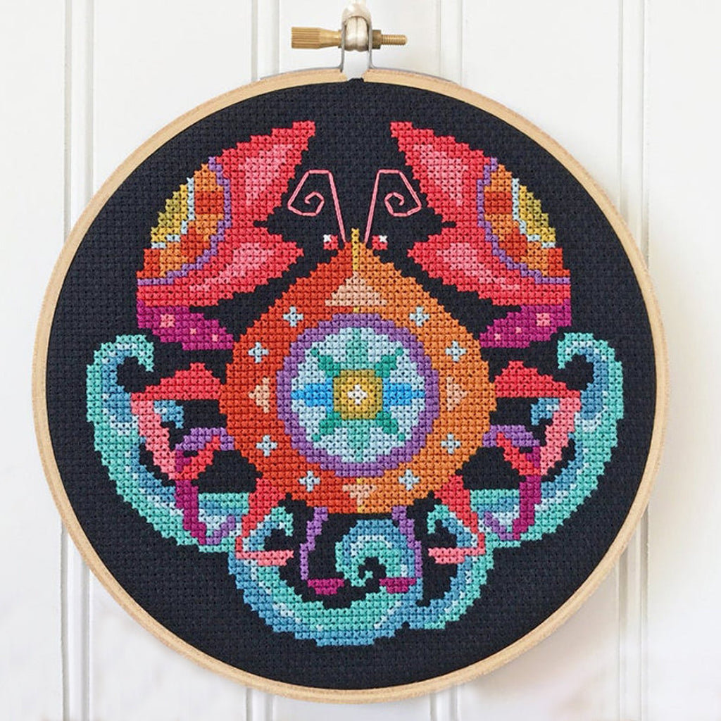 Black Aida cloth cross stitch hoop featuring a colorful crab zodiac design with pink antennae.