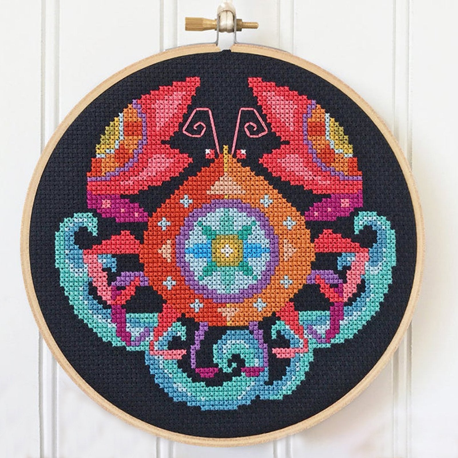 Black Aida cloth cross stitch hoop featuring a colorful crab zodiac design with pink antennae.