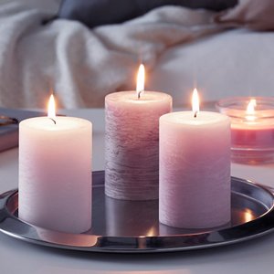 Three lit pillar candles of varying sizes and textures on a silver tray, with a blurred background of a couch and blanket.