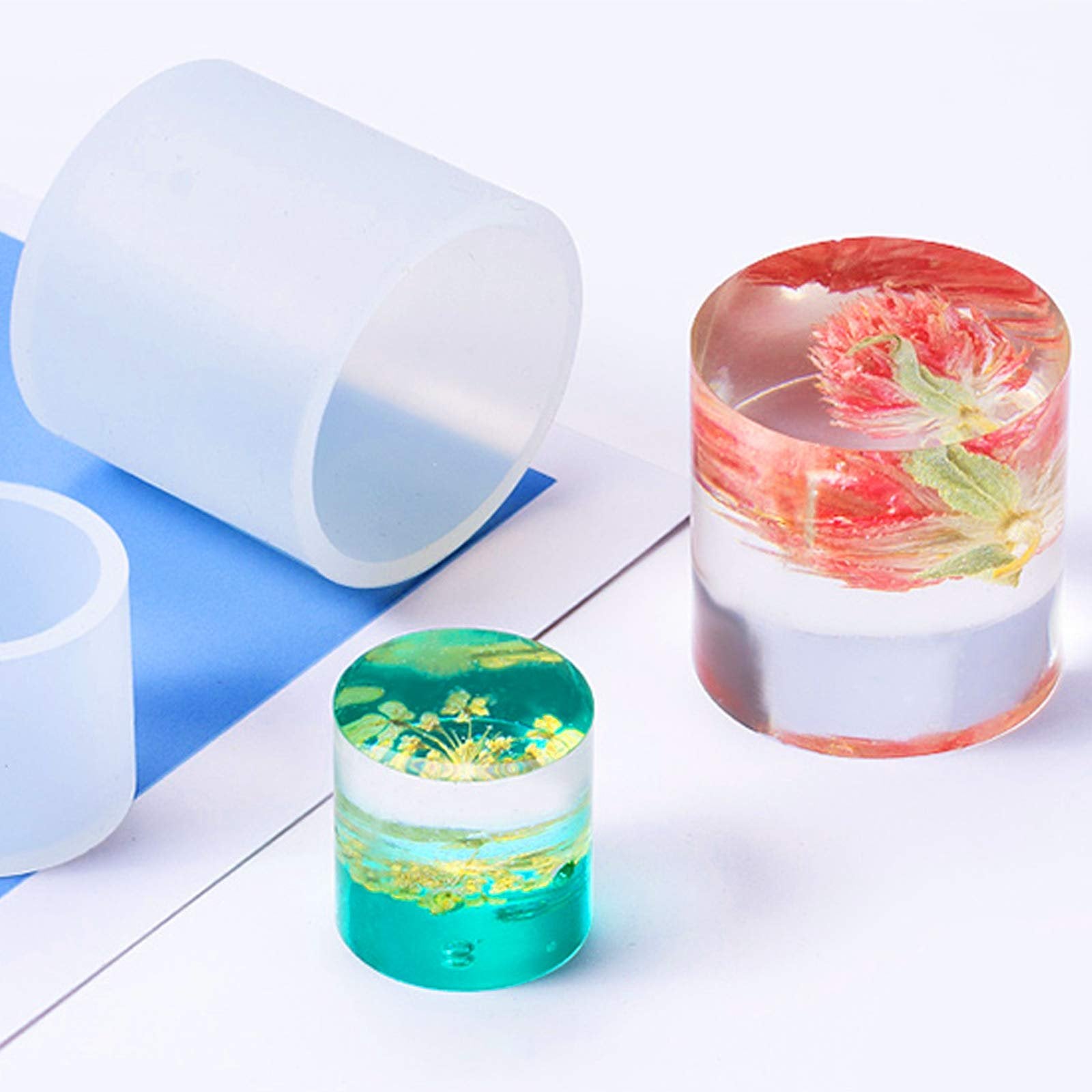Cylindrical silicone molds and finished resin crafts with flowers and gold flakes on a white and blue background