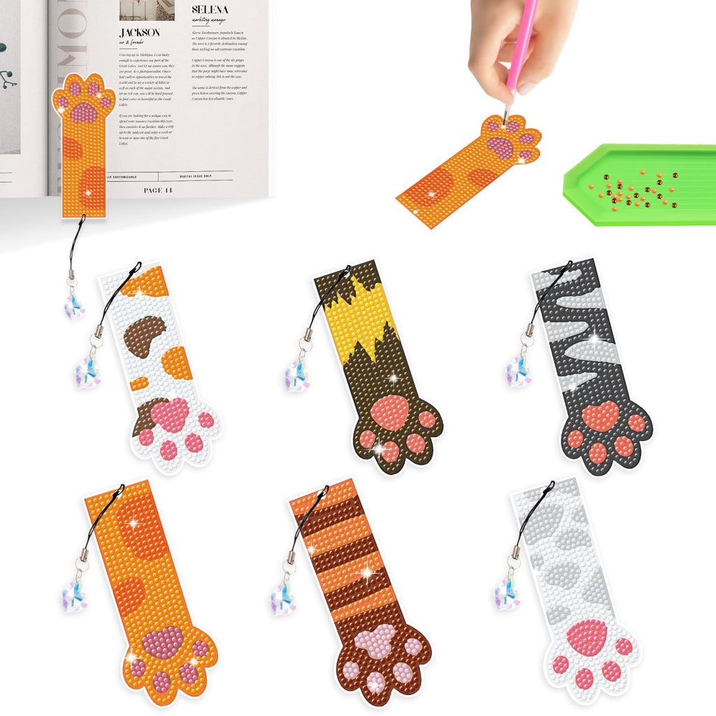Six diamond painting cat paw bookmarks with crystal pendants and a tray of beads, with one being assembled.
