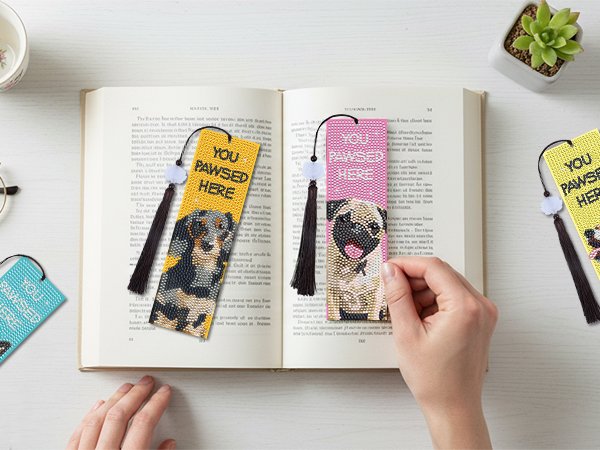 Diamond art bookmarks with dog portraits and tassels placed in an open book.