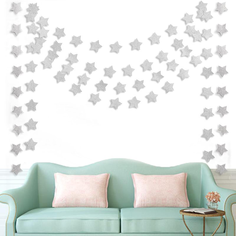 Silver glitter star garland draped on a wall above a teal sofa with pink pillows
