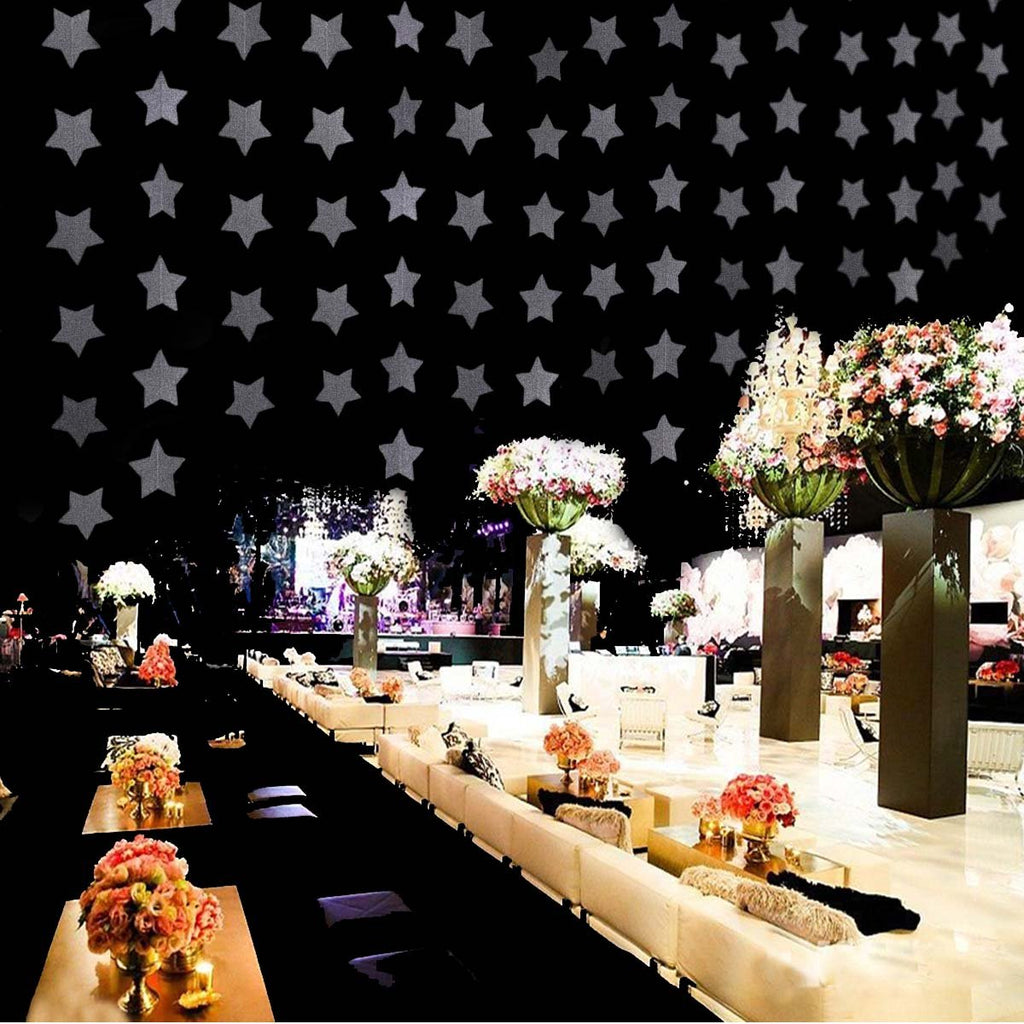 Glitter silver star garland draped across a black ceiling above a decorated event space with seating and floral arrangements.