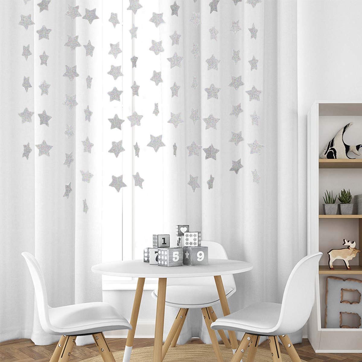 Glitter silver star garland hanging on white curtains above a small table with chairs and decorative blocks.
