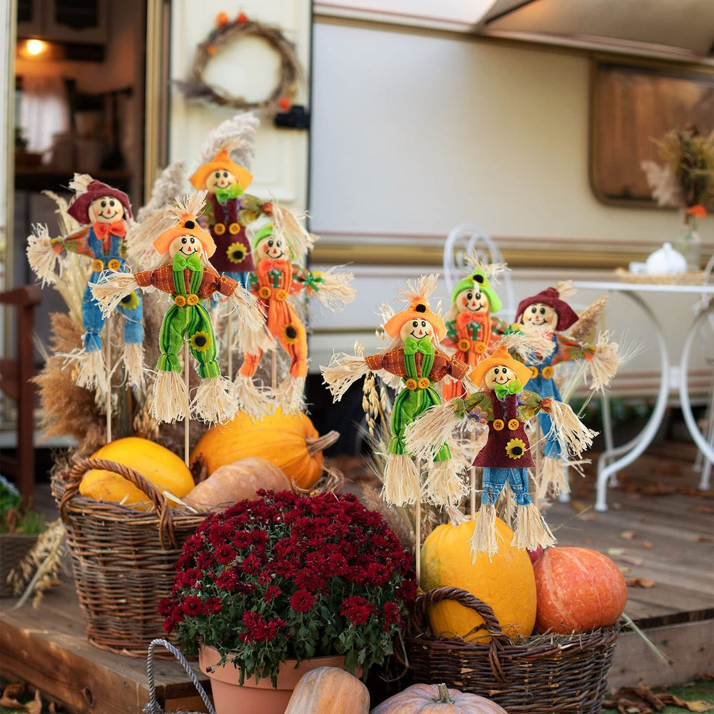 Group of six decorative scarecrows with straw accents and button details, arranged with pumpkins and fall foliage on a wooden porch.