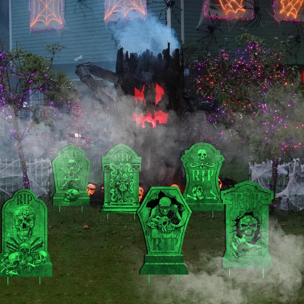 Halloween tombstone yard signs with skulls and RIP text glowing green on a lawn with spooky decorations