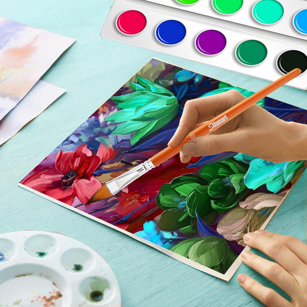 Hand holding an orange watercolor brush painting a colorful floral artwork, with a paint palette and watercolor pans nearby.