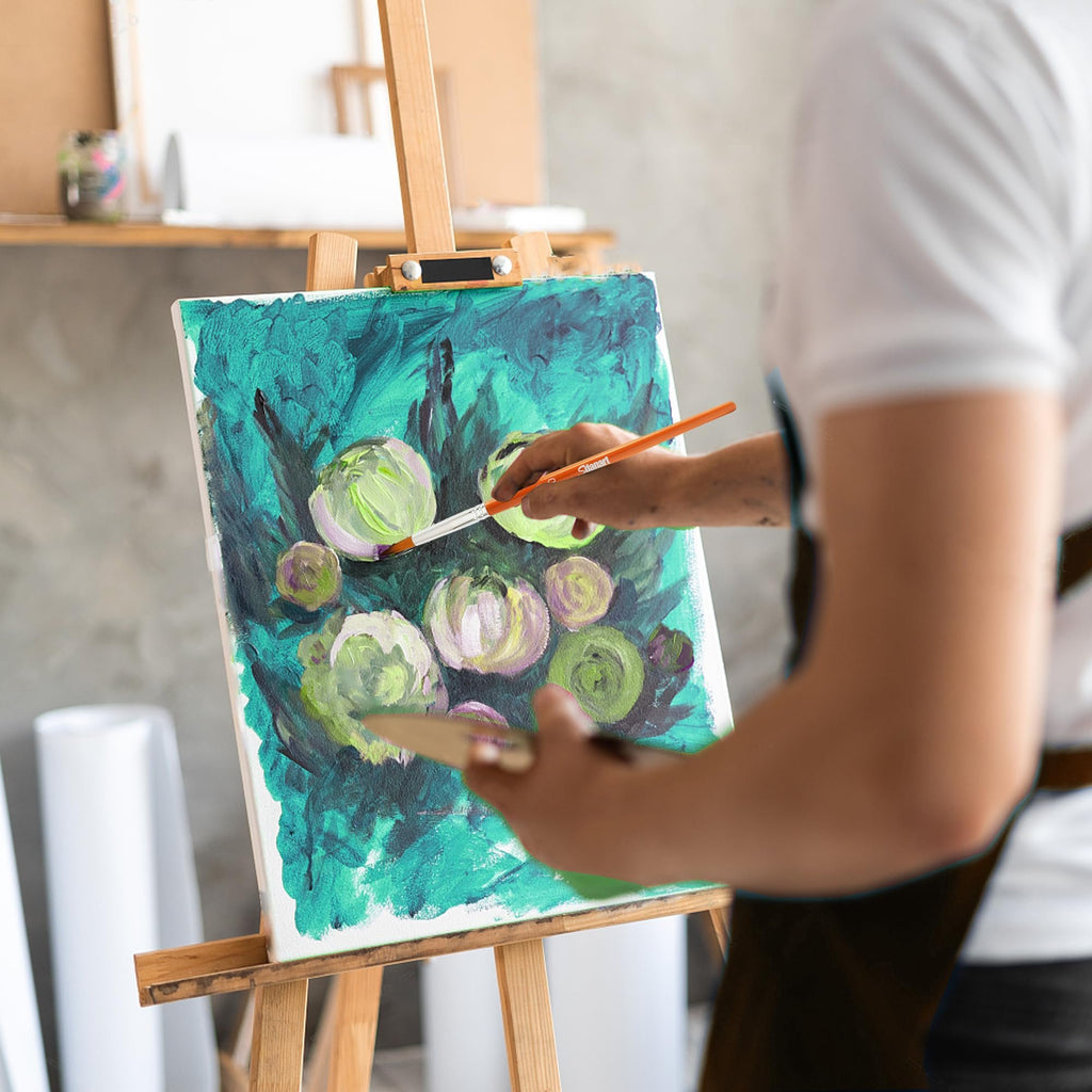 Artist painting on canvas with watercolor brushes and palette, close-up on hand holding brush