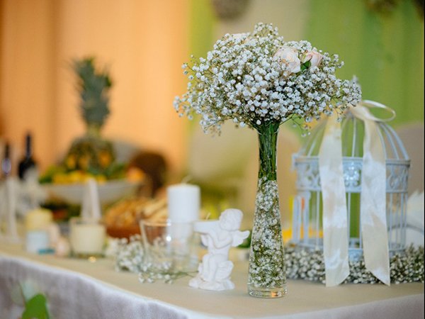 White baby's breath bouquet in a glass vase on a decorated table with a birdcage and pineapple centerpiece