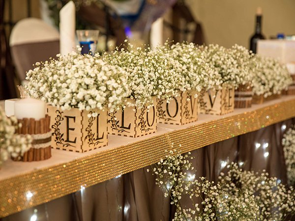 Table centerpiece with white baby's breath flowers in wooden boxes spelling LOVE, decorated for an event.