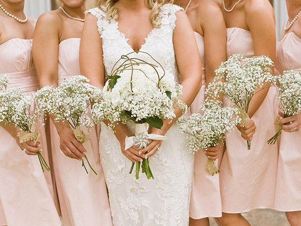 Bride and bridesmaids holding bouquets of white baby's breath flowers with burlap ribbon