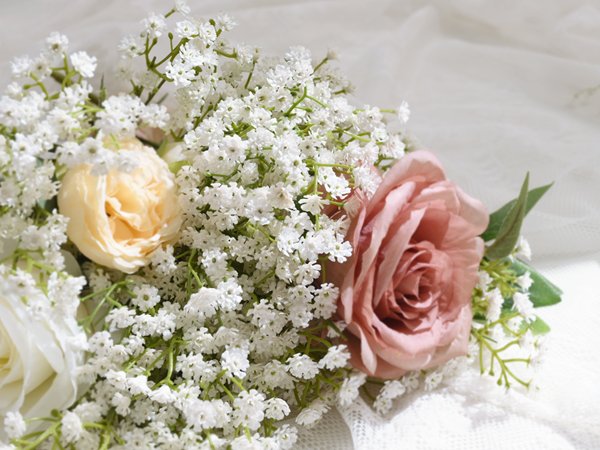 Close-up of a bouquet of artificial baby's breath and roses, featuring pink and cream roses with delicate white flowers.