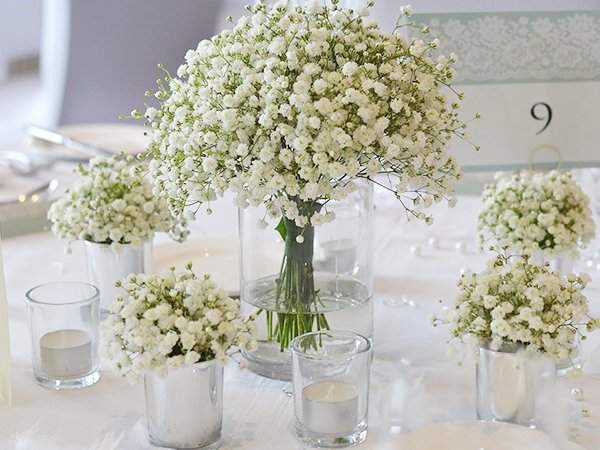 Table setting with multiple arrangements of white baby's breath flowers in vases and votive candles.